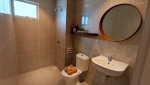 Modern bathroom with round wooden framed mirror above a sink and a black floating shelves at Daffodil Residency Puncak Alam